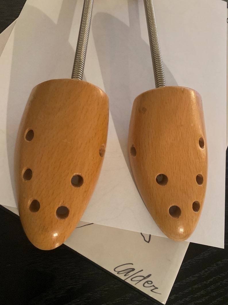 May include: A pair of wooden shoe trees with metal spring mechanisms. The shoe trees are light brown and have multiple holes.