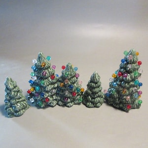 May include: A set of six green ceramic Christmas trees with colorful lights. The trees are different sizes and are arranged in a row.