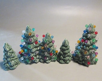Op de afbeelding: Een set van zes groene keramische kerstboompjes met kleurrijke lampjes. De boompjes zijn van verschillende grootte en zijn in een rij gerangschikt.