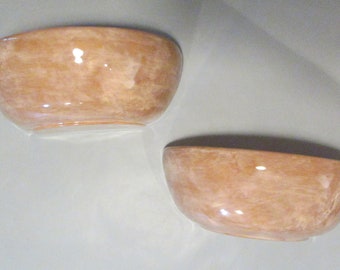 May include: Two ceramic bowls with a marbled glaze in a light brown color. The bowls are slightly oval shaped and have a glossy finish.