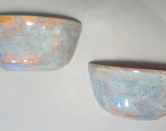May include: Two ceramic bowls with a light blue glaze and a subtle orange and pink marbling effect.