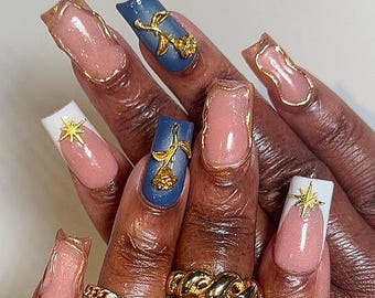 May include: Close-up of a hand displaying long, square acrylic nails. The nails are adorned with gold rose and star designs, and gold trim. The nails are painted in shades of pink, white, and blue, showcasing a detailed nail art design.