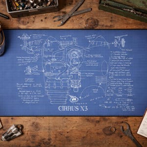 Peut inclure: Un tapis de bureau bleu avec un plan d'ingénierie de moteur et le texte "CIRRUS X3". L'image montre un bureau avec des outils, un carnet, une tasse de café et un casque argenté sur une surface en bois.