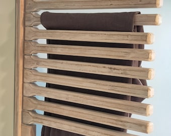 May include: A wooden wall-mounted towel rack with a brown towel hanging on it. The rack has a light wood finish and is made of multiple slats.