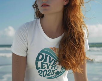 May include: White t-shirt with a round graphic that says "DIVE LEYTE 2025" in teal and white, with a sun and diver illustration. The model is wearing green shorts and has long red hair.
