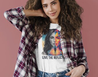 May include: White t-shirt featuring a split-face graphic with a woman's portrait, half in grayscale and half in vibrant colors. The text "LIVE THE REFLECTION" is below the graphic. The person is wearing a plaid shirt and blue jeans.