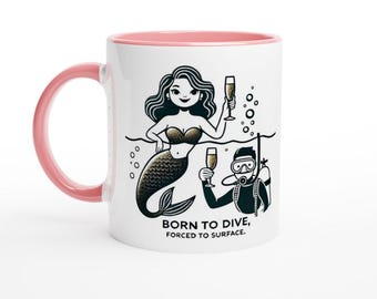 May include: White ceramic mug with a pink rim. The mug features a black and white illustration of a mermaid with a glass of champagne and a scuba diver with a glass of champagne. The text on the mug reads "Born to Dive, Forced to Surface."