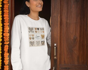 May include: White long-sleeve shirt with a square graphic of various heart designs in brown and black. The text "Love is a Lifestyle" is also on the shirt. The person is wearing purple pants and standing in a doorway.