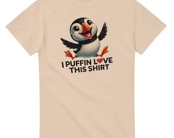 Może przedstawiać: Beżowa koszulka z kreskówkowym maskotką pingwina z czerwonym sercem i napisem "I puffin love this shirt".