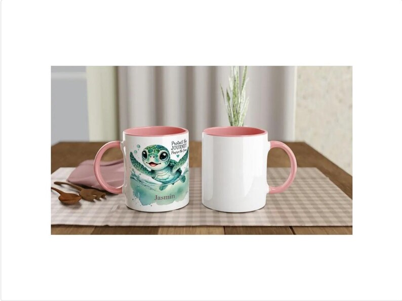 Może przedstawiać: Dwa ceramiczne kubki o pojemności 310 ml z r&oacute;żowymi brzegami. Jeden kubek przedstawia zielonego ż&oacute;łwia morskiego z tekstem "Chroń podr&oacute;ż, chroń morze" i imieniem "Jasmin". Drugi kubek jest pusty.