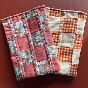 May include: Two quilted fabric cases. One is a patchwork of dusty rose and floral patterned squares with a brass snap closure. The other is a patchwork of orange and white gingham squares with a silver snap closure.