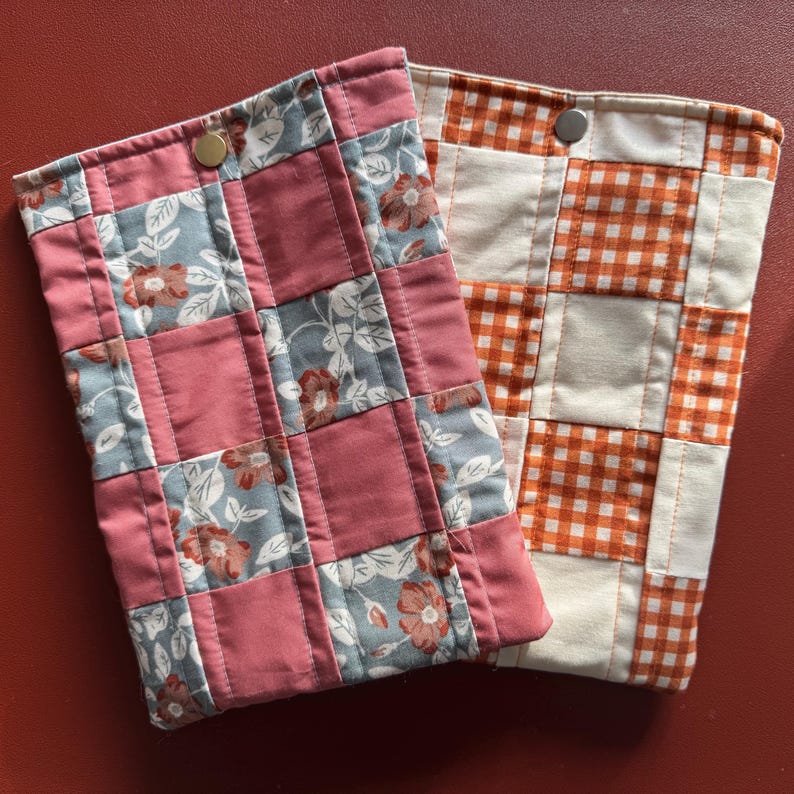 Puede incluir: Dos fundas de tela acolchada. Una es un patchwork de cuadrados de color rosa polvoriento y con estampado floral con cierre de bot&oacute;n a presi&oacute;n de lat&oacute;n. La otra es un patchwork de cuadrados de cuadros vichy naranja y blanco con cierre de bot&oacute;n a presi&oacute;n plateado.