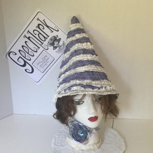 May include: A purple and white striped hat with ruffles. The hat is made of fabric and has a pointed top. The hat is sitting on a mannequin head with brown hair.