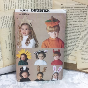May include: A sewing pattern for children's Halloween costumes. The pattern includes nine different costumes: a sunflower, a cow, a devil, a skunk, a reindeer, a bunny, a pumpkin, a star, and a witch. The pattern is from Butterick and has the number 6304 on it.