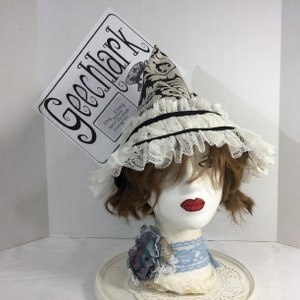May include: A white and black patterned hat with a wide brim and lace trim. The hat is tilted at an angle and has a small, white sign attached to it that says "Geekmark" with the text "Etsy, Flickr, Twitter, Facebook, Instagram" underneath.