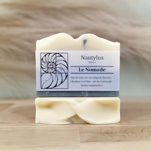 Puede incluir: Una pastilla de jabón con un diseño de remolino gris y blanco. El jabón está etiquetado como "Nautylus Skincare Le Nomade" y describe el jabón como un jabón todo en uno para el cuerpo y el cabello con carbón activado, sal marina y aceites esenciales.