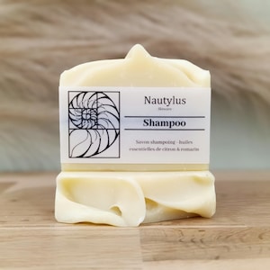 Puede incluir: Una barra de jabón de champú blanco con una etiqueta que dice "Nautilus Skincare Shampoo Savon shampooing - huiles essentielles de citron & romarin"