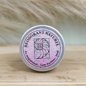 Peut inclure: Une boîte en argent avec une étiquette rose et blanche qui indique "Deodorant Naturel Au Magnesium - Sans Parfum - 30ml". L'étiquette présente un motif de coquillage stylisé.