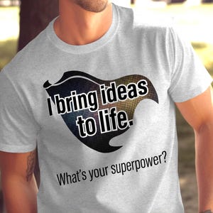 May include: Light gray t-shirt with a graphic design. The design features a shield shape with the text "I bring ideas to life." and "What's your superpower?" in black and white.