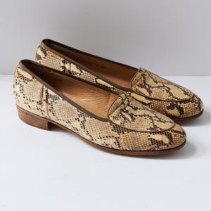 May include: A pair of brown and beige snakeskin loafers. The loafers have a pointed toe and a low heel.