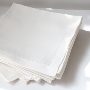 May include: A stack of white linen napkins with a delicate stitched border.