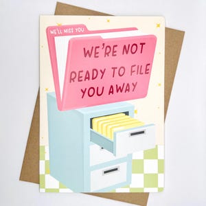 May include: A greeting card featuring a pink file folder illustration with the text "WE'RE NOT READY TO FILE YOU AWAY." A light blue filing cabinet with an open drawer revealing yellow files is also shown. The background is light yellow with a checkered pattern.