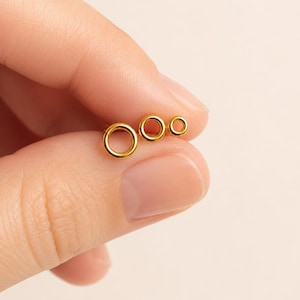 May include: Three small, circular gold-toned rings of varying sizes arranged in a horizontal row. Each ring features a smooth, polished surface and a simple, continuous band design. The rings are presented in a graduated sequence from largest to smallest.