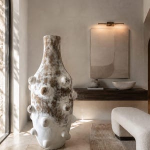 Puede incluir: Un jarrón de cerámica alto de suelo con un acabado texturizado y moteado en marrón y blanco. El jarrón presenta una serie de protuberancias redondeadas en su superficie, un cuello estrecho y un cuerpo ancho y redondeado que se estrecha hacia la base.