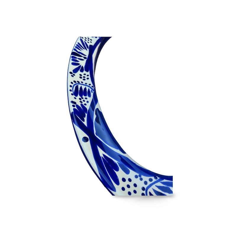 May include: A curved, ceramic bracelet with a blue and white floral pattern. The bracelet features a glossy finish and a detailed design of stylized leaves and dots. The color scheme is a classic combination of deep blue and white.