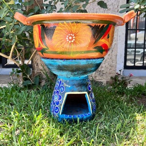 Puede incluir: Una maceta de terracota pintada a mano con una base azul y blanca. La maceta tiene un diseño floral y es perfecta para plantar flores o hierbas.