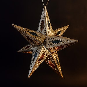 May include: A decorative star-shaped ornament with a metallic gold finish, suspended by a thin wire. The star features intricate cut-out patterns and is accented with red and blue colored panels, creating a festive and elegant appearance. The background is a dark, solid color.
