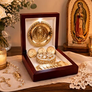 Op de afbeelding: Een donkerhouten presentatiedoos met een goudkleurige ronde plaquette met een reliëf van een religieuze figuur, een centrale ronde houder ingelegd met heldere kristallen en diverse goudkleurige munten op de witte fluwelen voering.