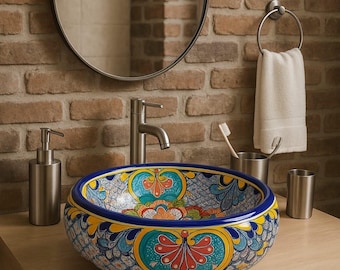 May include: A decorative, hand-painted ceramic vessel sink with a vibrant floral design in blue, yellow, and red. The sink is set on a light wood vanity with a stainless steel faucet and accessories, against a brick wall.