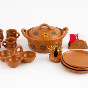May include: A terracotta-coloured ceramic cookware set. The set includes a lidded pot, small cups, plates, a condiment dish, and a napkin holder. Floral designs decorate the pot and napkin holder. The set is ideal for serving food.