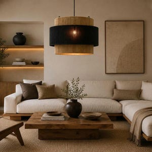 May include: A cylindrical pendant light fixture featuring a three-tiered design with two natural tan woven bands at the top and bottom, separated by a central black fabric band, suspended from a thin black cord in a living room setting.