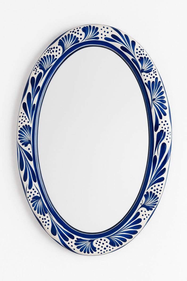 May include: Oval mirror with a blue and white floral design. The frame is a deep blue with a white border featuring a repeating pattern of stylized leaves and dots. The mirror has a reflective surface.
