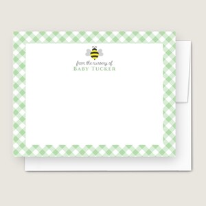 May include: A set of stationery featuring a light green gingham border. The stationery includes a white card with a cartoon bee and the text "from the nursery of BABY TUCKER". The stationery is placed on top of a white envelope.