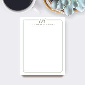 May include: A white notepad with a decorative border and the text "H THE HENLEY FAMILY" in a serif font. A cup of coffee and a succulent plant are in the background.
