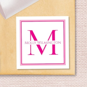 May include: A white square label with a pink border. The letter "M" is in a large pink font, with the text "MOLLY WILMINGTON" centered below the letter.