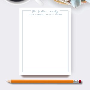 May include: A white notepad with a light blue border and the text "The Tucker Family" at the top. The names Jacob, Rachel, Molly, and Tucker are listed below. An orange pencil with a pink eraser rests at the bottom.