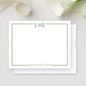 May include: White stationery card with a green border, the initials "E&B" at the top, and the word "WILMINGTON" at the bottom. The card is on top of a white envelope, with a white background and a ribbon.