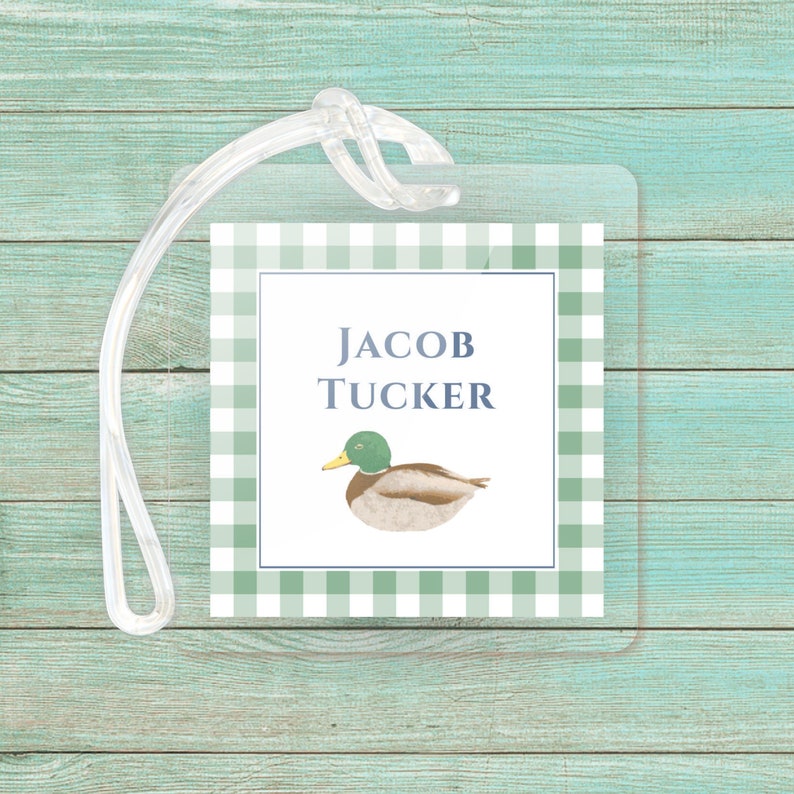 May include: A green and white gingham luggage tag with a duck illustration and the text 'JACOB TUCKER'.