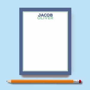 May include: A rectangular notepad with a white center, a thin light green border, and a thick dark blue outer frame. The name JACOB OLIVER is printed in dark blue and light green at the top. An orange pencil with a silver ferrule and pink eraser lies below.