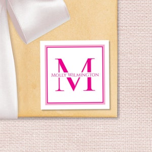 May include: A white square gift tag with a pink border. The tag features a large pink letter "M" with the text "MOLLY WILMINGTON" above it.