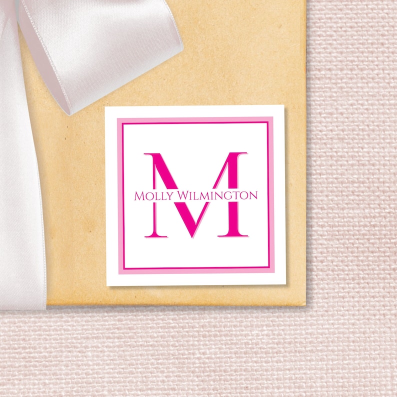 May include: A white square gift tag with a pink border. The tag features a large pink letter "M" with the text "MOLLY WILMINGTON" above it.