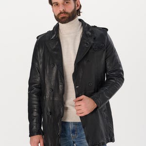 May include: A black leather jacket with a double-breasted design. The jacket has a classic trench coat style with a notched collar and button closures. The model is wearing a beige turtleneck and blue jeans.