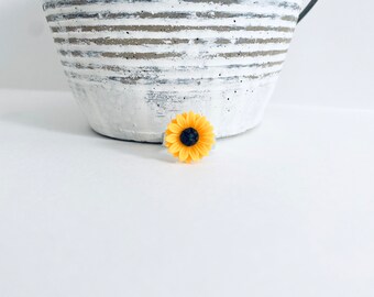 Könnte beinhalten: Ein gelber Sonnenblumenring mit schwarzem Zentrum. Der Ring liegt auf einer weißen Oberfläche.