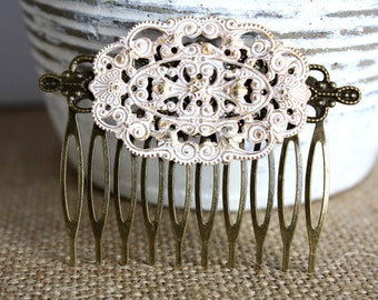 May include: A white and gold filigree hair comb with a decorative design. The comb has a row of teeth on the bottom.