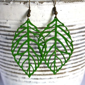 Puede incluir: Un par de pendientes de hoja verde con un delicado diseño de corte. Los pendientes están hechos de metal y tienen un gancho de color bronce.