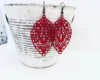 May include: A pair of red filigree earrings with a delicate, intricate design. The earrings are made of metal and have a dangling, teardrop shape.